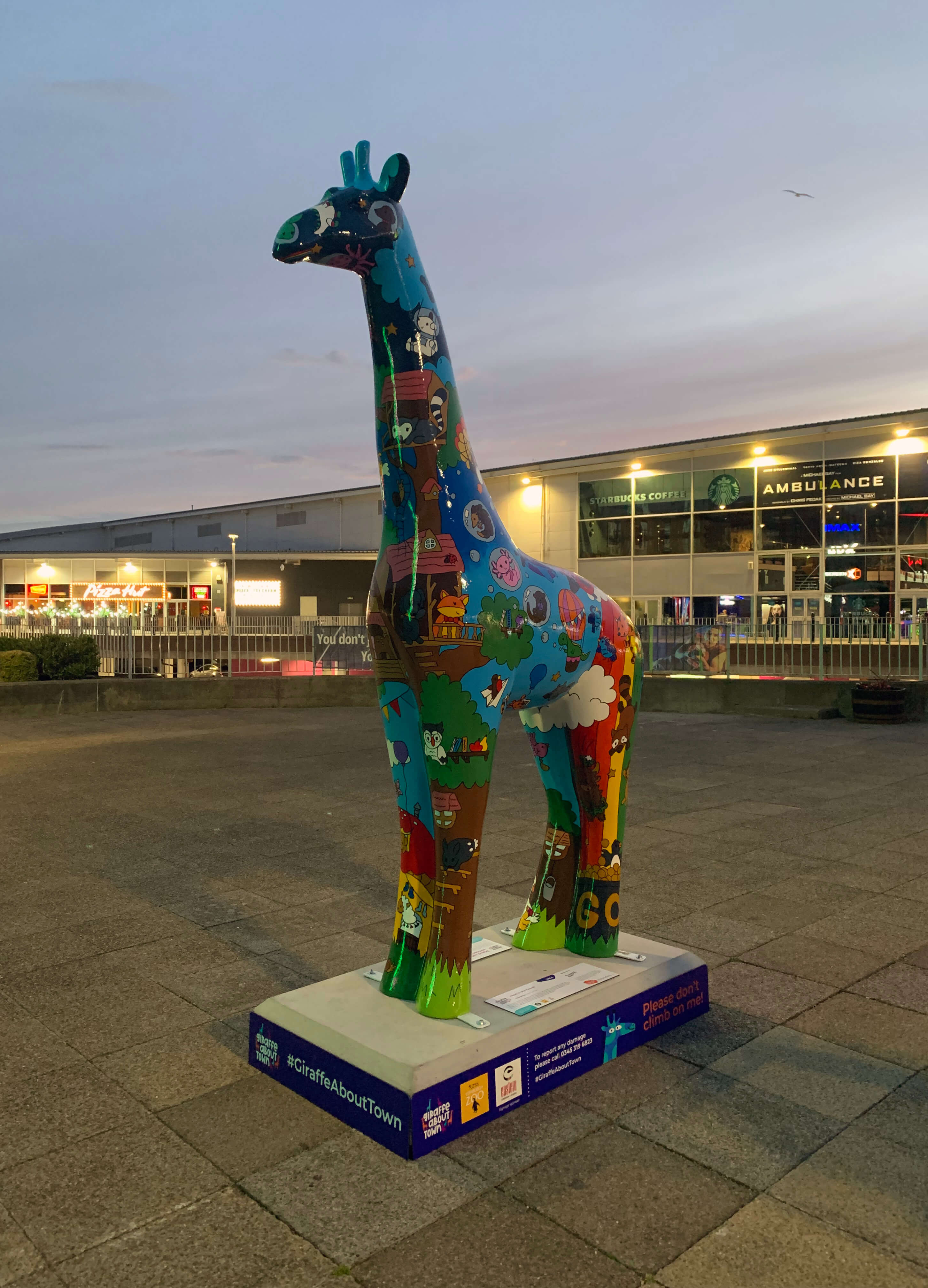 a painted giraffe statue standing outside an entertainment park at sunset