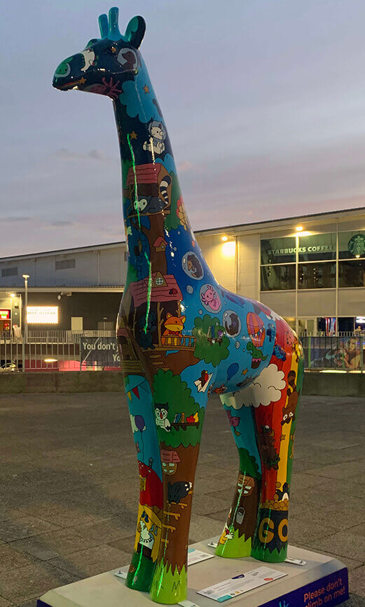 a painted giraffe statue standing outside an entertainment park at sunset